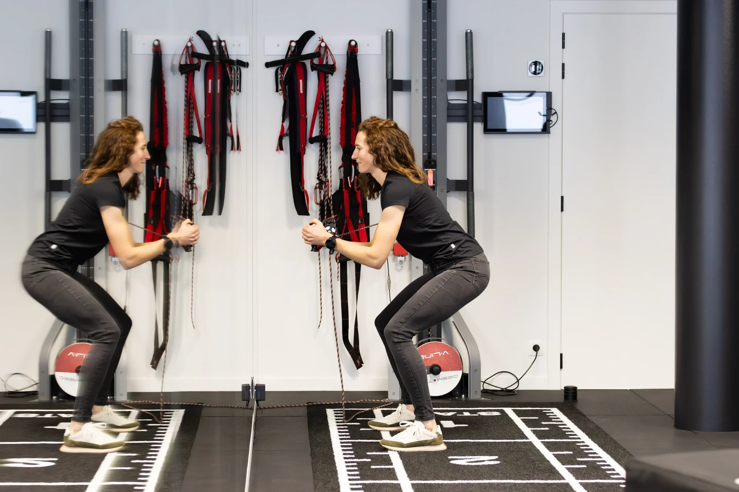 Elise Farrazijn traint aan de kabeltoestellen in de trainingsruimte van MOOOV, gespiegeld in de spiegelwand