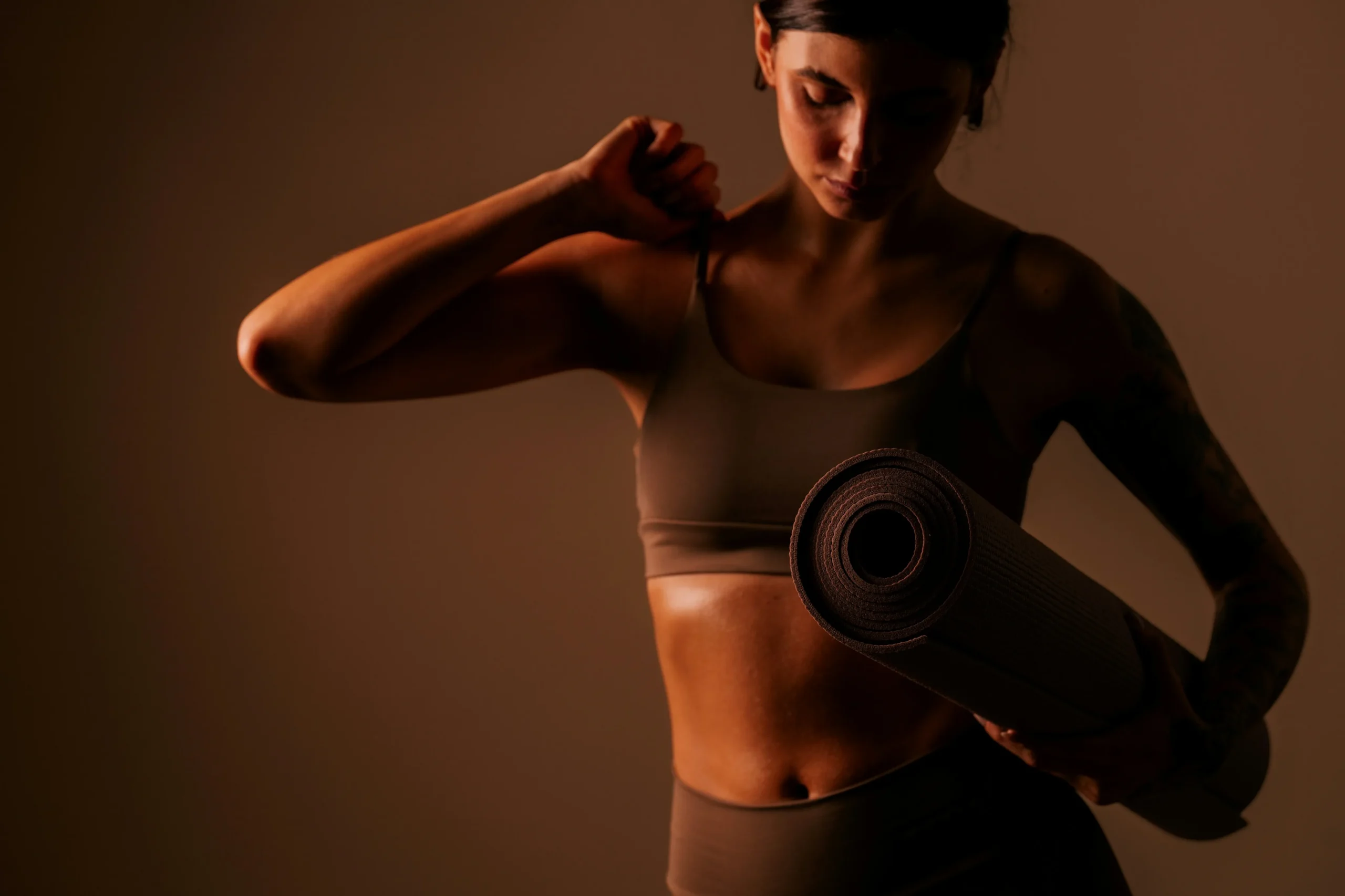 Sportieve vrouw in sportkleding met een opgerolde fitnessmat onder de arm
