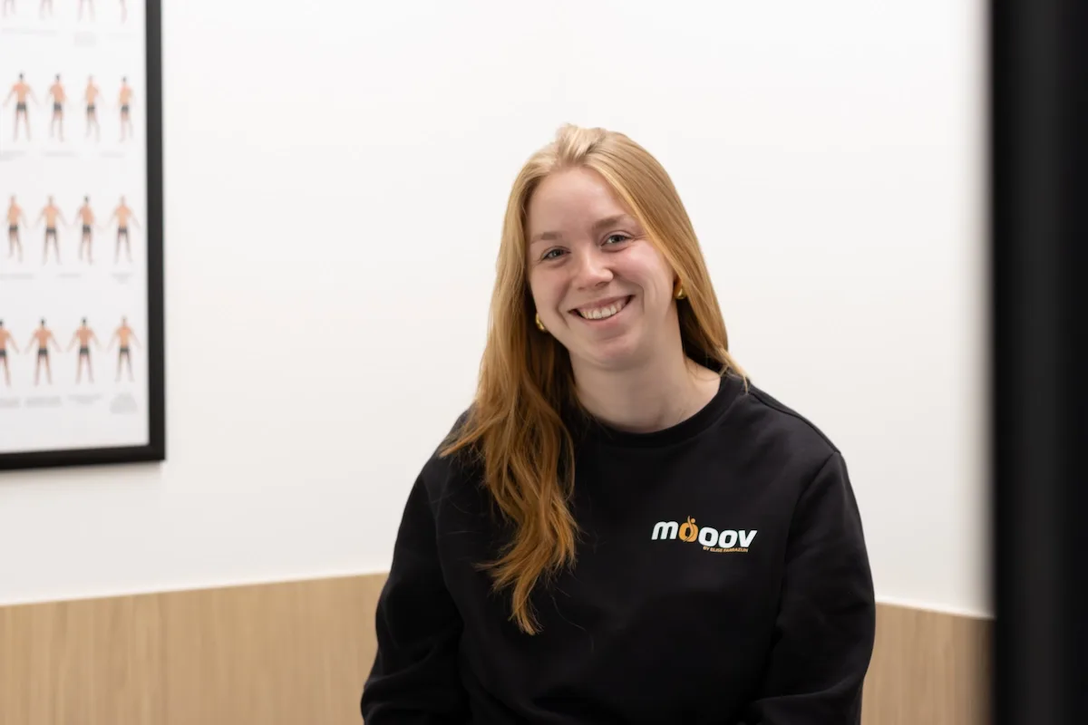Lana Coene lacht in de praktijkruimte van MOOOV, met een anatomieposter aan de muur