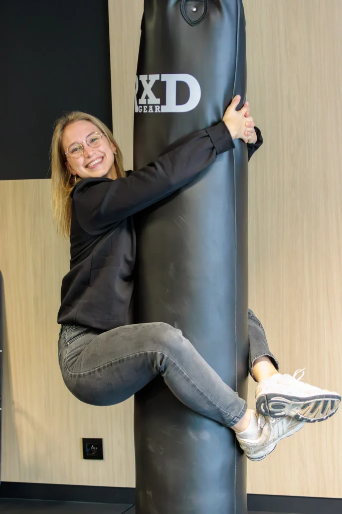 Lisa Vandierendonck hangt lachend aan een bokszak in de trainingsruimte van MOOOV