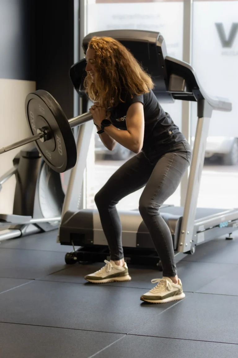 Vrouw doet een squat met een halterstang voor een loopband