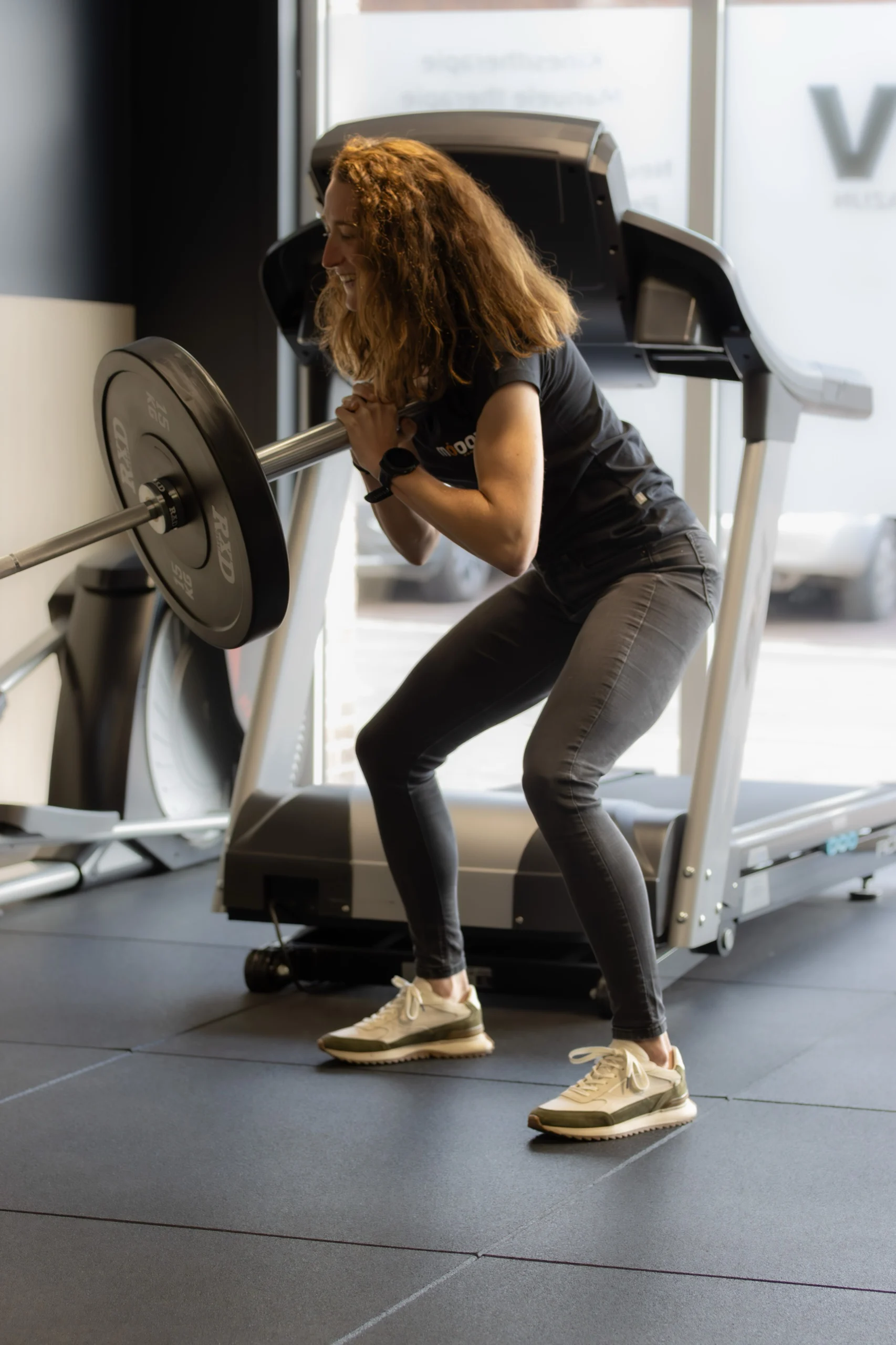 Vrouw doet een squat met een halterstang voor een loopband