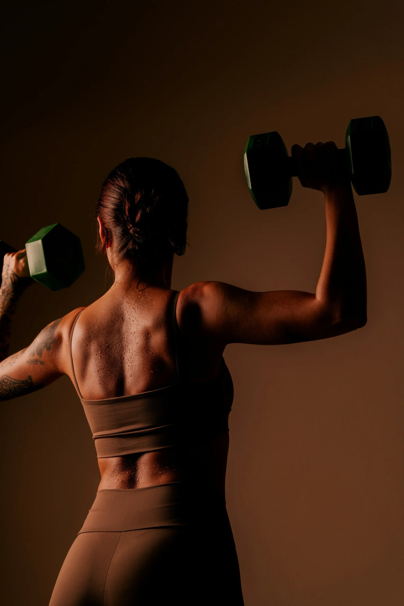 Vrouw traint haar schouders met twee dumbbells, van achteren gezien