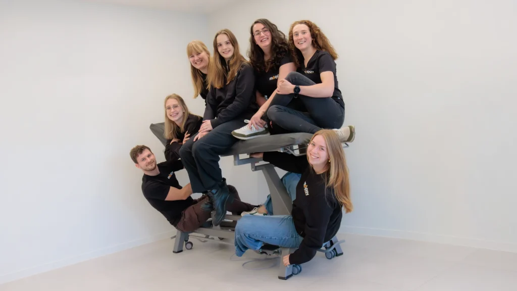 Het team van MOOOV zit en hangt lachend samen rond een behandeltafel